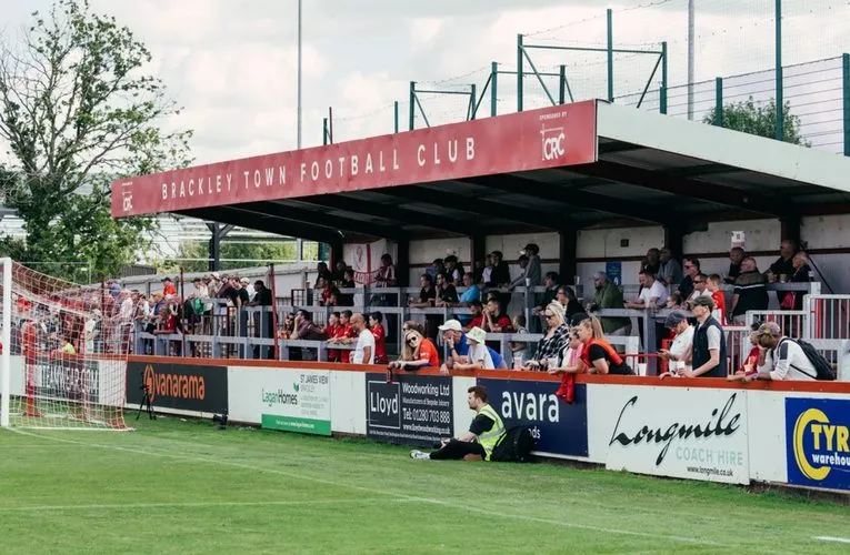 Khung cảnh sôi động của sân St James Park Brackley trong một ngày có trận đấu, với các cổ động viên tập trung trên khán đài